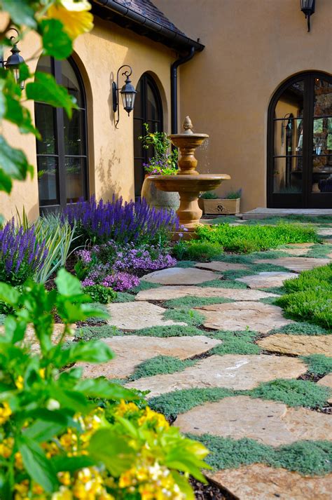 a stone path in front of a house with flowers and greenery on either side