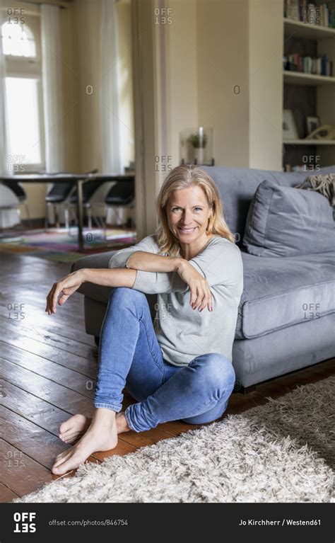 Portrait of smiling mature woman siiting barefoot on the floor in the living room stock photo ...