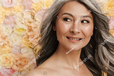 Smiling mature topless woman standing posing over floral wall background, looking aside People ...