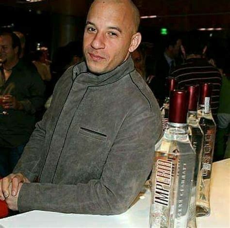 a man sitting at a table with bottles of alcohol in front of him and people behind him