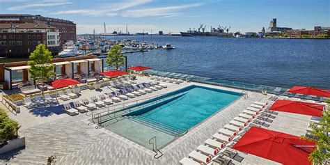 an outdoor swimming pool with red umbrellas next to the water and boats ...