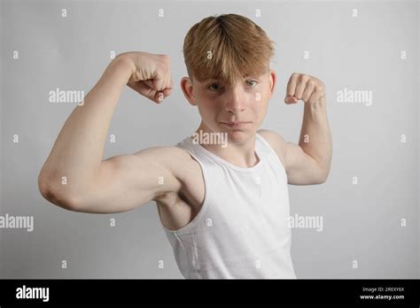 Portrait of a 14 year old caucasian teenage boy wearing a sleeveless vest flexing both his ...