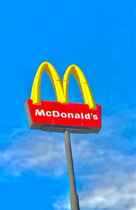 a mcdonald's restaurant sign in front of a blue sky with clouds behind it