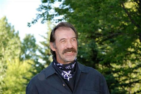 a man standing in front of trees wearing a bandana and smiling at the camera