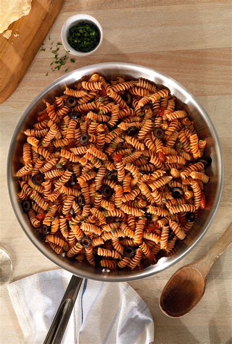 a pan filled with pasta on top of a wooden table next to a knife and spoon