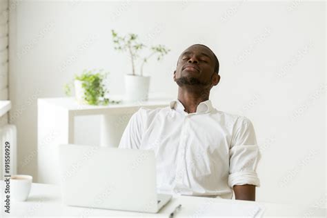 African office worker relaxing with eyes closed sitting at work desk with laptop, black employee ...