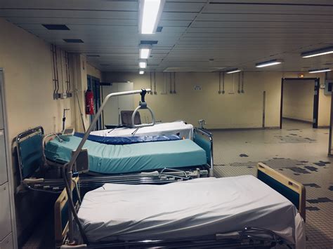 These images show a vast and derelict space with few hospital beds pushed to the side. The ...