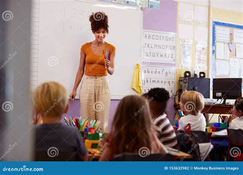 Female Teacher Standing at Whiteboard Teaching Maths Lesson To Elementary Pupils in School ...