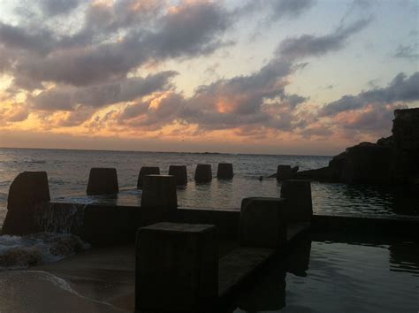 the sun is setting over the ocean with rocks in the water