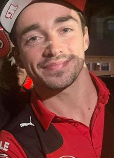 a man in a red shirt and hat smiling at the camera with other people behind him