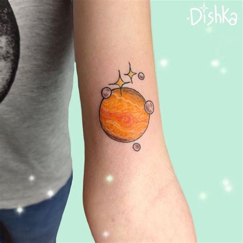 a small tattoo on the arm of a person with an orange planet and stars ...