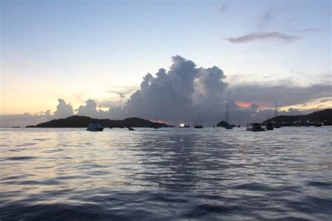 several boats floating in the water at sunset with clouds above them ...