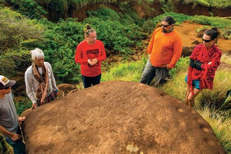 four people standing on top of a large rock