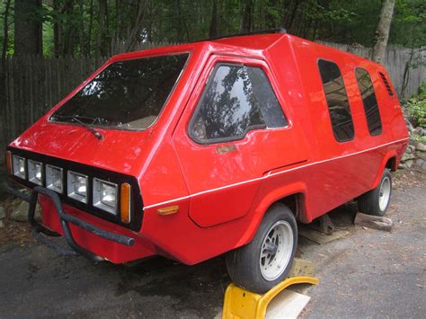 a red car parked on the side of a road next to a yellow traffic cone