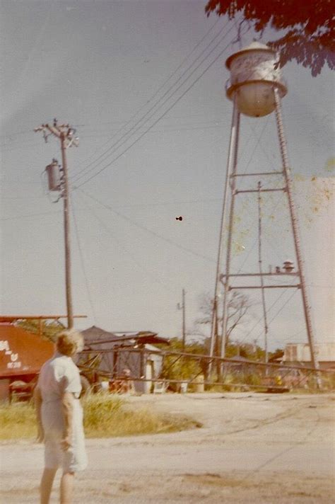 an old photo of a man standing in front of a water tower and looking up at the sky