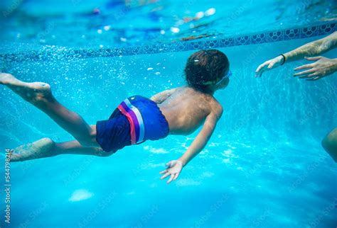 Young diverse boy swimming underwater in a swimming pool. Learning to ...