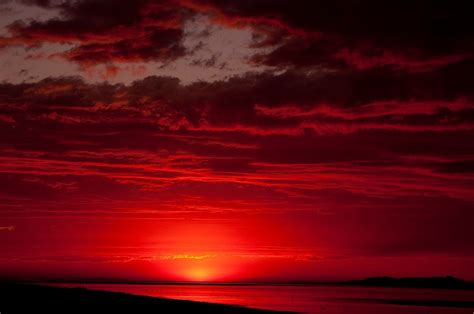 the sun is setting over an ocean with red clouds