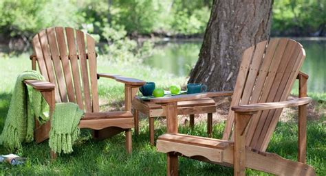 two wooden chairs sitting in the grass next to a tree with a blanket on it