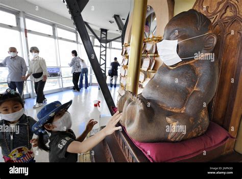 OSAKA, Japan - A child touches the feet of a mask-wearing wooden statue ...