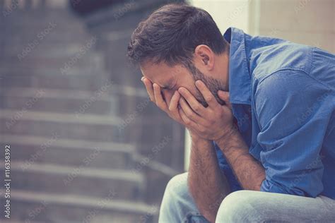 stressed sad young crying man sitting outside holding head with hands Stock Photo | Adobe Stock