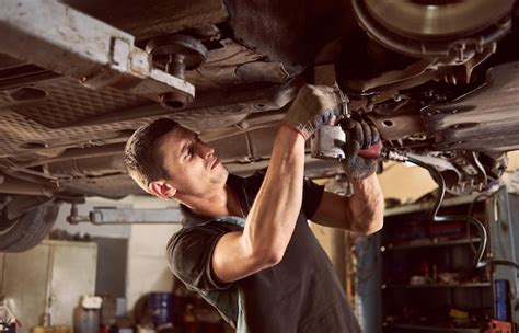 Premium Photo | Repair man fixing car in repair station under lifted car during repair in garage