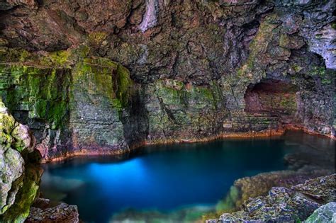 a blue pool in the middle of a rocky area with green moss growing on it