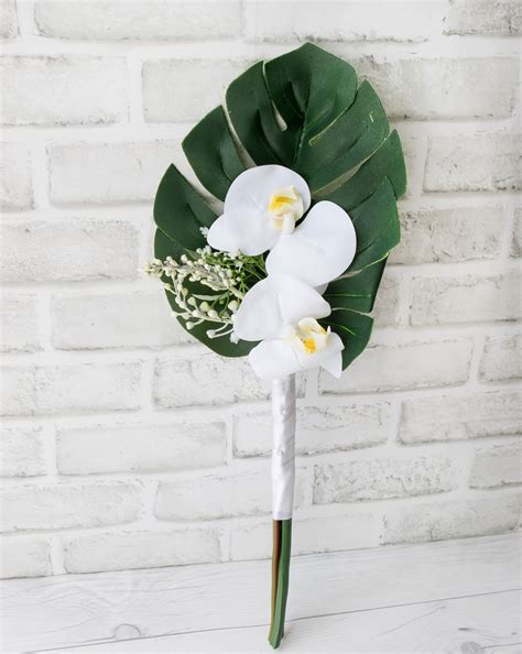 a bouquet of white orchids and greenery on a wooden table next to a ...