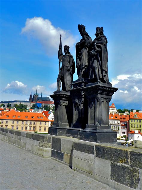 two statues on the edge of a bridge with buildings in the background and blue sky