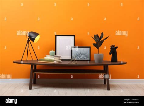 Wooden coffee table with different decor near orange wall indoors. Stylish interior design Stock ...