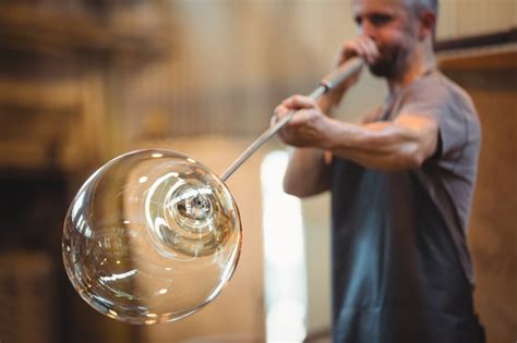 Free Photo | Glassblower shaping a glass on the blowpipe