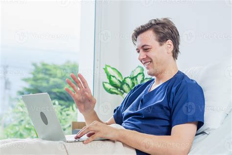 Caucasian patient using laptop in hospital room. man sick patient lying in a hospital bed ...