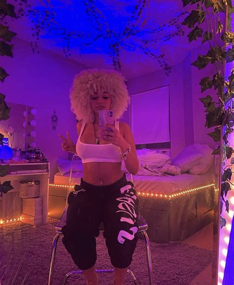 a woman sitting on a stool taking a selfie with her cell phone in a purple lit room