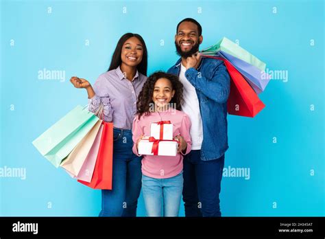 Holidays Gifts Shopping. Portrait of cheerful black family of three people holding bright ...