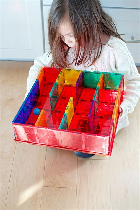 Little girl playing with a maze made of magnetic tiles and trying to get a ball through the maze ...