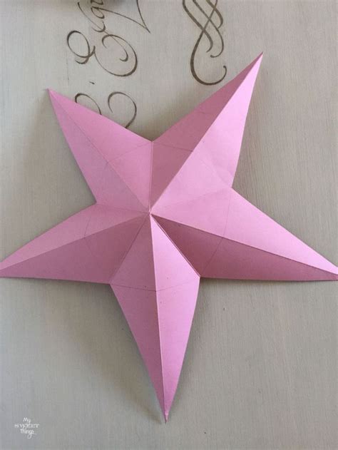 a pink origami star on a table with some scissors and thread next to it