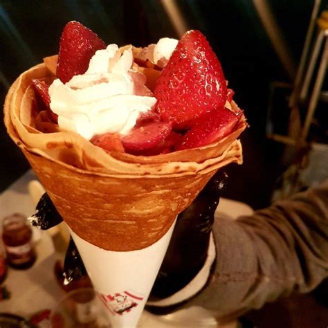 a person is holding up a dessert cone with strawberries and whipped ...