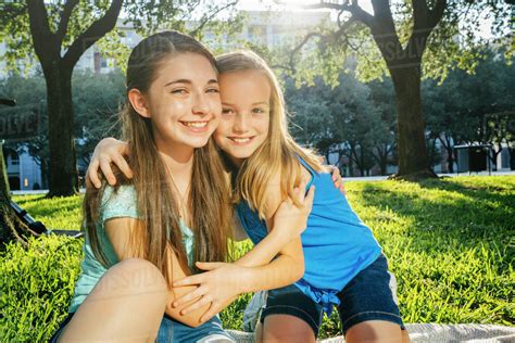 Portrait of smiling Caucasian sisters hugging in park - Stock Photo - Dissolve