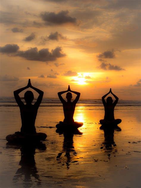 three people sitting on the beach doing yoga exercises at sunset with their arms in the air