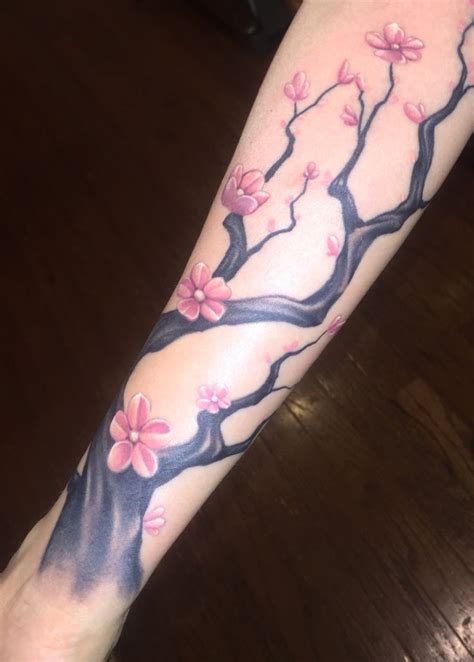 a woman's arm with pink flowers on it and a tree in the background