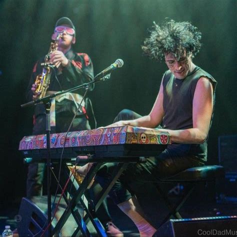 two men playing musical instruments on stage at a music festival, one with curly hair and the ...