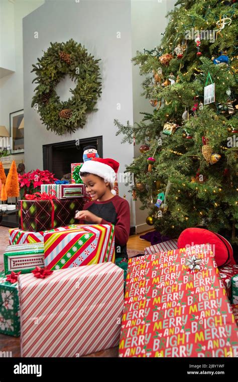 Child sitting by a Christmas tree unwrapping Christmas presents Stock Photo - Alamy