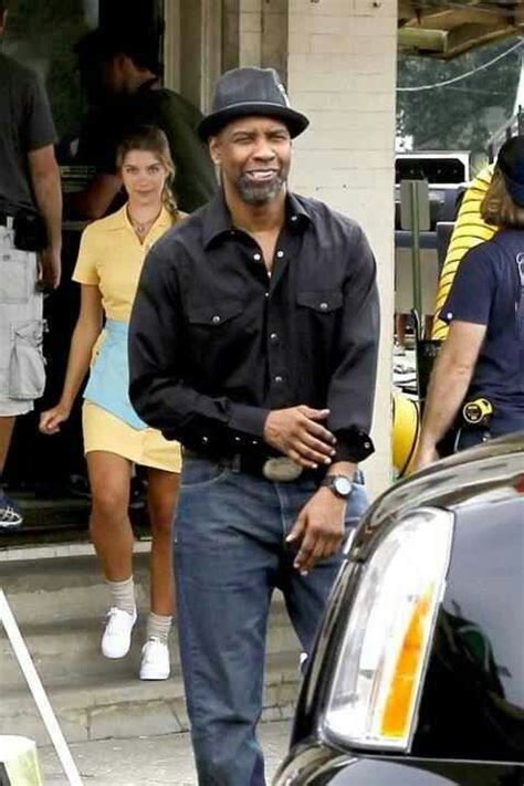 a man in a black shirt and hat standing next to a car