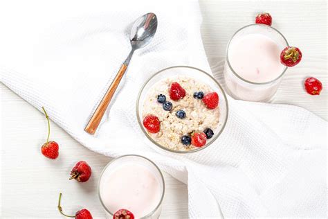 Oatmeal with strawberries and blueberries and yogurt on the white table. Top view - Creative ...