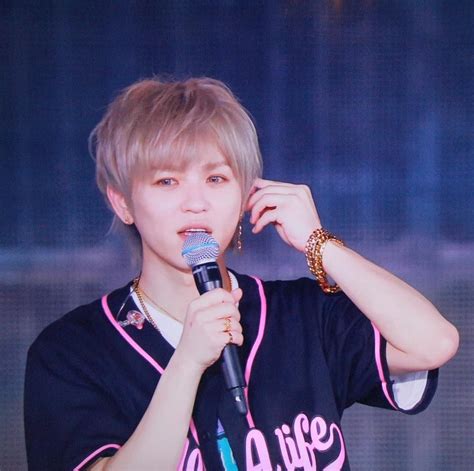 a man holding a microphone up to his ear while wearing a black shirt with pink writing on it