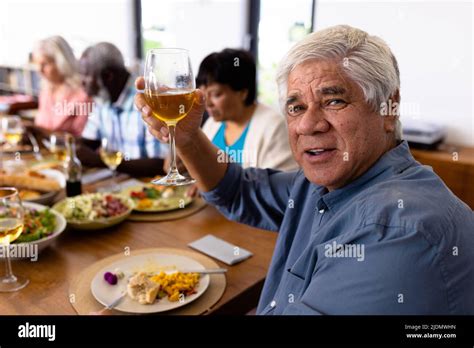 Portrait of multiracial senior man enjoying wine while having lunch with friends at dining table ...