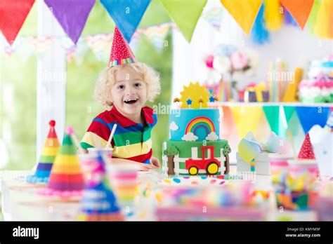 Kids birthday party. Child blowing out candles on colorful cake. Decorated home with rainbow ...