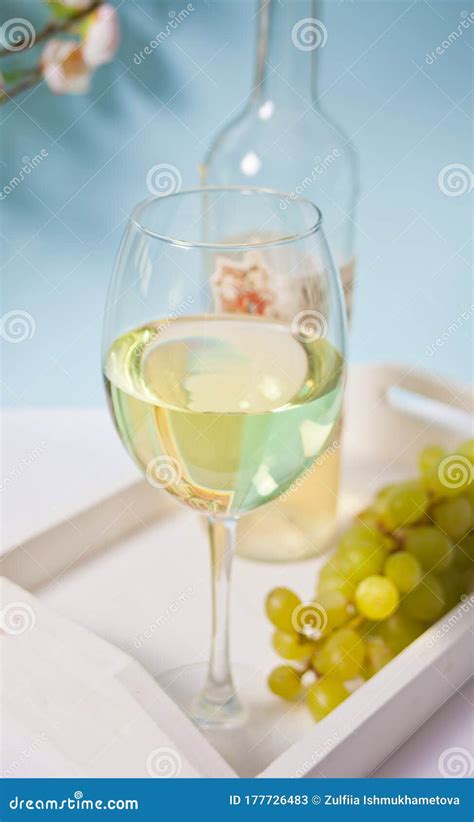 Glass and Bottle with White Grape Wine with Grapes Under a Blooming Branch. Romantic Spring ...
