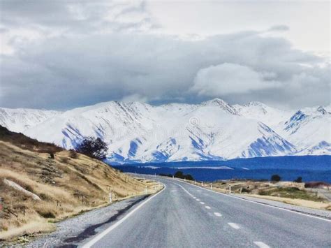 A Mountain Road Leading To a Snow Covered Range and Grey Moody Sky ...