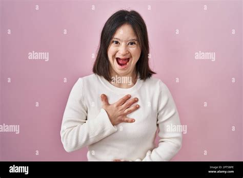 Woman with down syndrome standing over pink background smiling and ...