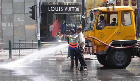Reinigung einer Straße in Thailand, Louis Vuitton Shop im Hintergrund ...